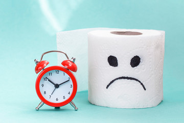 Constipation, indigestion, digestion problem. Alarm clock and toilet paper on light background....