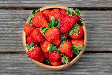 Sweet fresh juicy organic ripe strawberries in wooden bowl on wooden surface outdoors