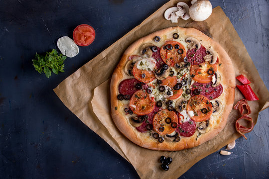 Hot pizza, cheese, bacon, tomatoes, sausage on a dark Board. and the improvised flag of Italy