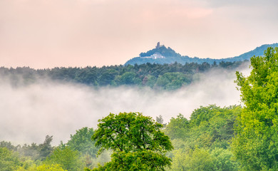 Fog arise from a valley after an evening rain shower in spring, view onto the hill Drachenfels in Siebengebirge, a hilly forest landscape in Germany