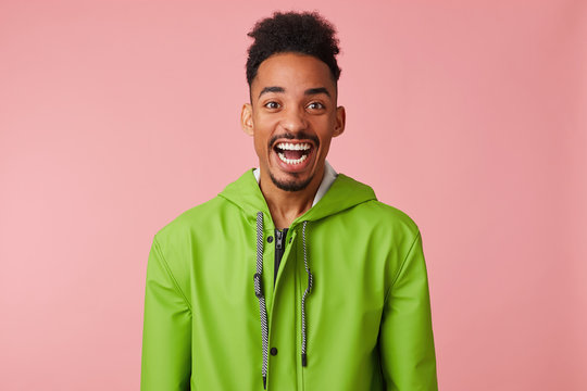 Close up of young happy amazed african american handsome guy broadly smiles, looks at the camera in surprise with wide open mouth, stands over pink background.
