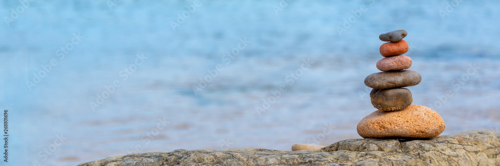 Wall mural pile of pebbles on a beach, panoramic blue water background, balanced stack of stones with copy spac