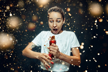 Woman drinking a cola at studio. Young smiling happy caucasian girl opening can with cola and enjoying the spray. Advertising image about favourite drink. Lifestyle and human emotions concept.