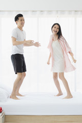 Lovely Asian couple jumping on bed in bedroom..