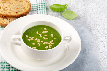 The concept of a healthy, vegetarian or dietary food: cream spinach soup, with pine nuts and basil. With slices of vegetarian carrot bread. On a light background