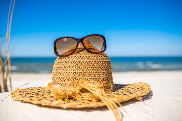 Summer beach accessories - sun hat and sunglasses on sand. Summer vacation background, Baltic Sea, Poland.