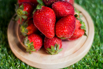 Red strawberries in a wooden plate on green grass with blue sky background