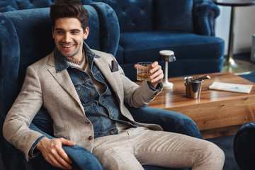 Young business man sitting in chair indoors in office drinking alcohol.