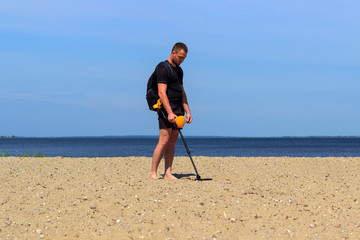 guy in shorts with a metal detector walking on the beach