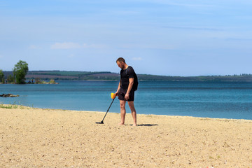 young man with metal detector on sandy beach