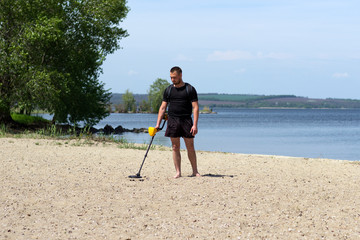 young man with metal detector on the beach