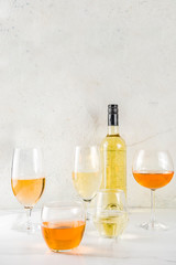 Trendy orange wine, with white wine in different glasses, white concrete background copy space
