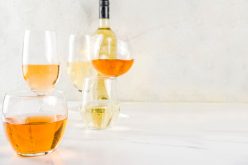 Trendy orange wine, with white wine in different glasses, white concrete background copy space
