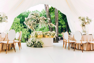 luxury wedding decor. Wedding in white and gold colors. elegant wedding decorated with white flowers. tropical flowers at the wedding. Wedding in a white tent. white table of the bride and groom.