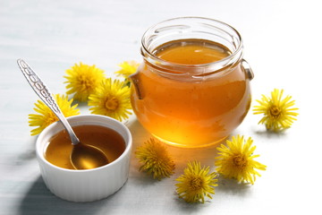 Dandelion jam in glass pot, bowl with spoon and yellow flowers on white background