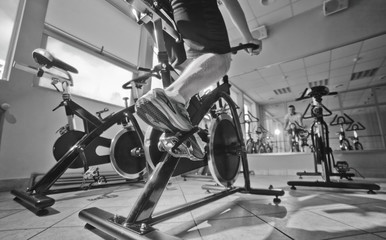 Fototapeta na wymiar Wide angle view of man in sports sneakers and shorts does exercises on cardio bike at spinning class. Healthy lifestyle concept