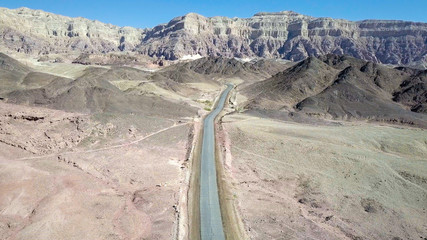 Long stretch of an old Desert road with mountains and blue sky in the background, Aerial image.