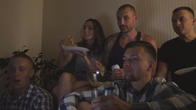 Happy Best Friends Watching Comedy Movie Or Social Media Video On Laptop At Home. Young Group Of People Drinking Cola And Eating Snacks While Looking Online Tv Show On Computer At Night. Slow Motion