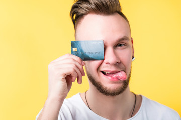 Young bearded hipster covering eye with credit card. Banking finance cashless payment. Man grimacing sticking out tongue