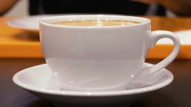 White mug with hot cappuccino coffee on the table. Steam rises up. Mug close up.