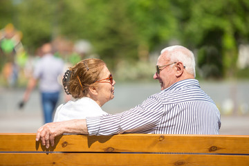 Senior couple wearing sunlglasses relaxing sitting on a bench in city park