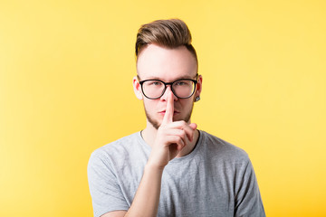 Shh be quiet secret silence gesture. Young man showing hush sign shushing finger on lips. Serious somber facial expression.