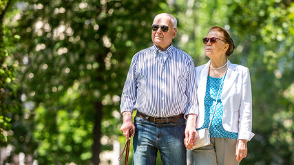Obraz premium Cheerful senior couple having good time in city park, walking, laughing and enjoying sunny day. Old people wearing color clothes ans sunglasses