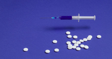 Medical minimalistic concept. Syringe, pills on blue background.