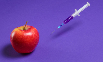 Genetically modified Red Apple with syringes on purple background, fruit concept minimal