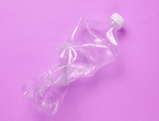 Minimalistic ecological concept. Crumpled plastic bottle on purple background. Environmental plastic pollution