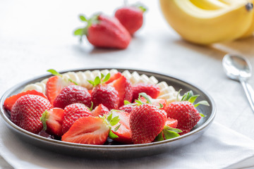 Salad of strawberries and banana on a dark plate on a light background. Served with Greek yogurt. Bananas and strawberries. 