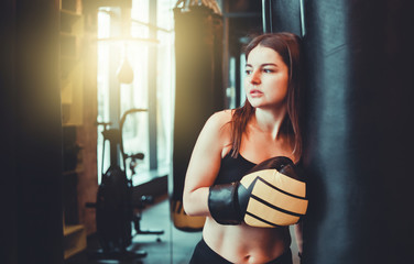 A tired young sport woman in boxing gloves  resting after  heavy boxing training with punching bag.