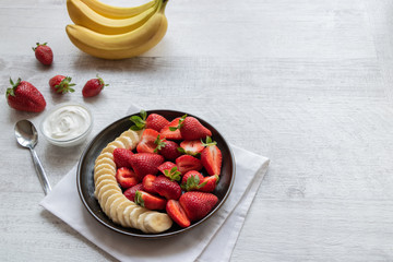 Salad of strawberries and banana on a dark plate on a light background. Served with Greek yogurt. Bananas and strawberries. Copy space..