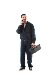 smiling workman in overalls talking on smartphone and holding toolbox isolated on white