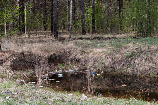 Pollution of nature. Garbage and plastic bottles float on the water of the reservoir inside the forest.