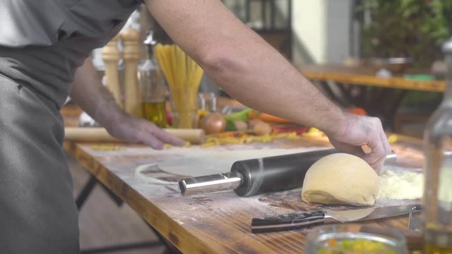 Chef cook sprinkling flour on pizza dough while rolling with roller pin. Man making dough for fresh pasta in italian restaurant. Cooking homemade pastry, cake and pie. Healthy homemade food.