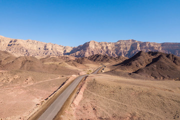 Fototapeta premium Long stretch of an old Desert road with mountains and blue sky in the background, Aerial image.