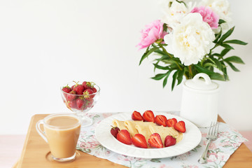 Fototapeta na wymiar pancakes with strawberries and coffee on the table near a vase with peonies on a white background