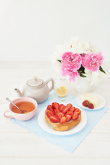 strawberry with croissant and tea on the table near a vase with peonies on a white background
