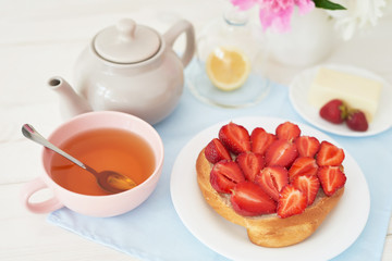 strawberry with croissant and tea on the table near a vase with peonies on a white background