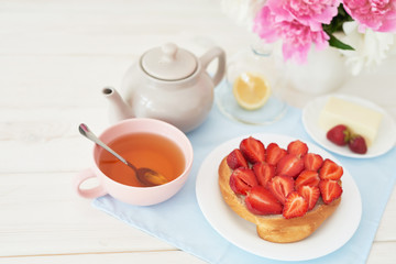 strawberry with croissant and tea on the table near a vase with peonies on a white background