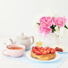 strawberry with croissant and tea on the table near a vase with peonies on a white background