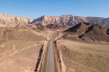 Long stretch of an old Desert road with mountains and blue sky in the background, Aerial image.
