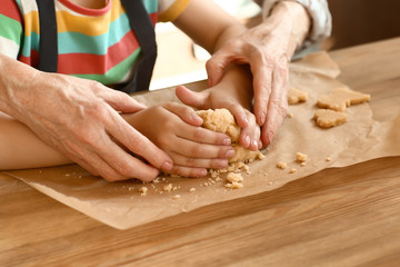 Little girl with her grandmother cooking cookies at table, closeup