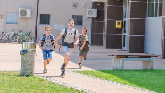 Three boys are running out of the school. Thy look happy because a school day is over. It's summer time.