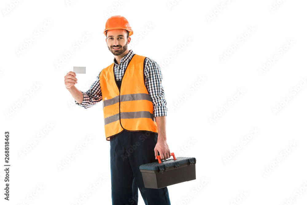 Wall mural cheerful construction worker with toolbox holding blank visit card and looking at camera isolated on white