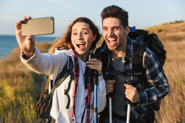 Cheerful young couple carrying backpacks hiking together