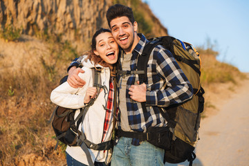 Cheerful young couple carrying backpacks hiking together