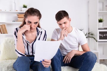 Happy couple reading mail and checking accountancy looking each other sitting on a couch at home