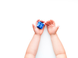 Child is holidng blue constructor block in fist. Kid's hands with toy on white background. Flat lay, top view, copy space.
